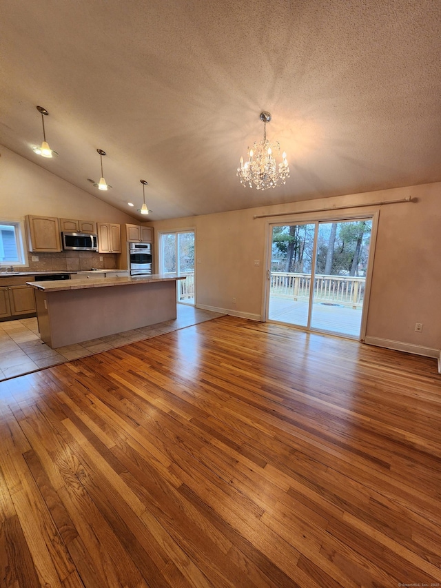 kitchen with open floor plan, light wood-type flooring, vaulted ceiling, stainless steel appliances, and a textured ceiling