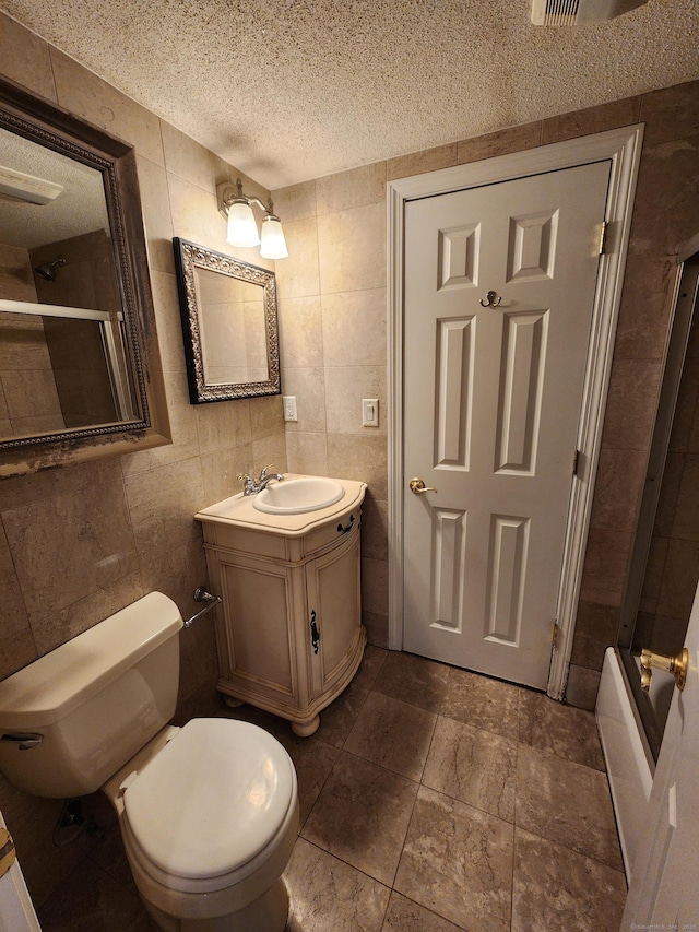 full bathroom with tile walls, toilet, vanity, shower / bath combination with glass door, and a textured ceiling