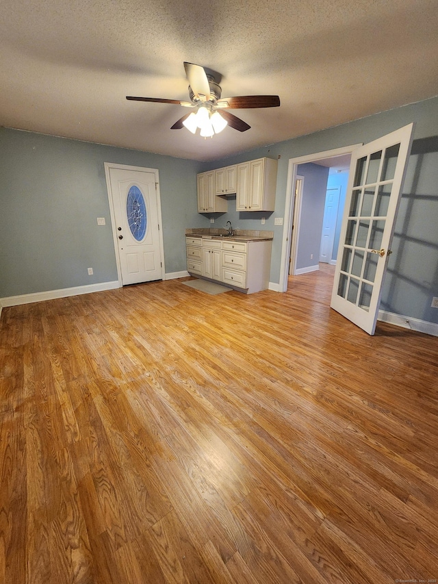 unfurnished living room featuring a sink, baseboards, a textured ceiling, and light wood finished floors