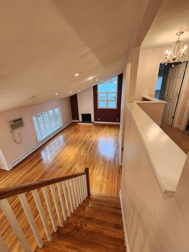 stairs featuring a wealth of natural light, lofted ceiling, a wall unit AC, and wood finished floors