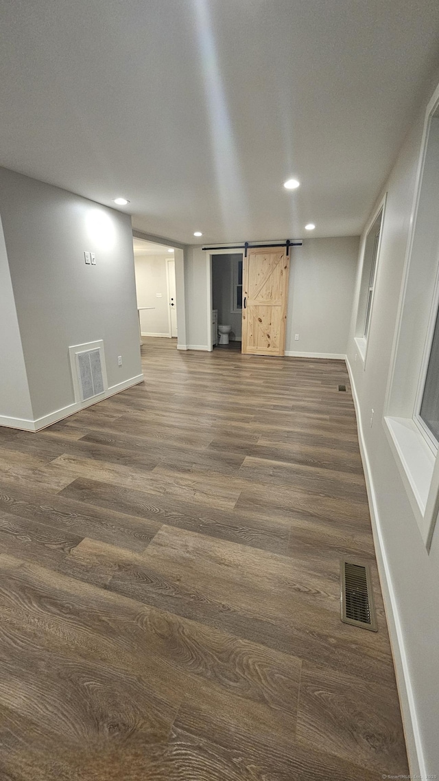 unfurnished living room with visible vents, baseboards, dark wood-type flooring, and a barn door