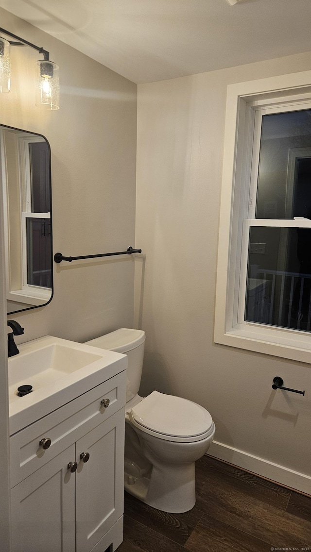 half bath with baseboards, toilet, wood finished floors, and vanity