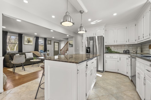 kitchen with a kitchen island, light tile patterned flooring, white cabinets, appliances with stainless steel finishes, and backsplash