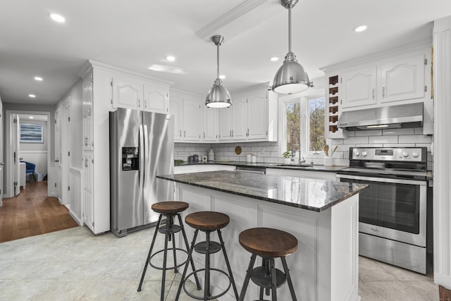 kitchen with stainless steel appliances, under cabinet range hood, white cabinetry, a kitchen breakfast bar, and tasteful backsplash