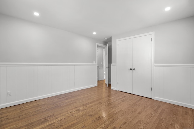 unfurnished bedroom with recessed lighting, a wainscoted wall, a closet, and wood finished floors