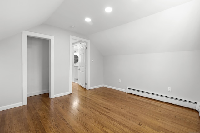 additional living space featuring wood finished floors, stacked washer / dryer, baseboards, baseboard heating, and vaulted ceiling