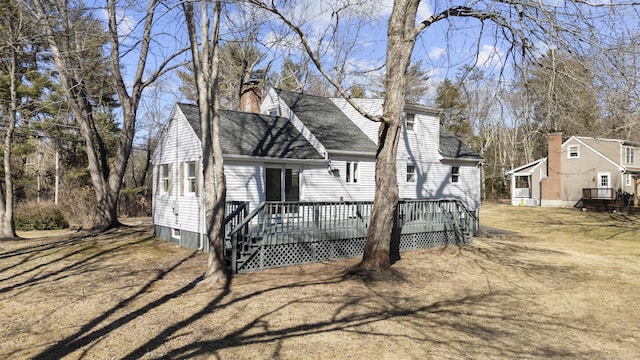 new england style home with a chimney, a deck, and a shingled roof