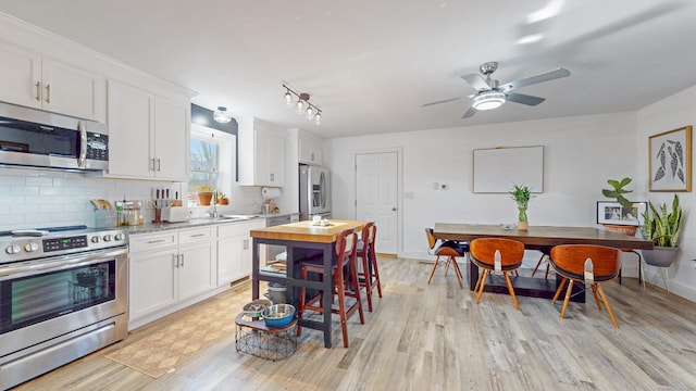 kitchen with decorative backsplash, white cabinets, appliances with stainless steel finishes, and light wood-style floors