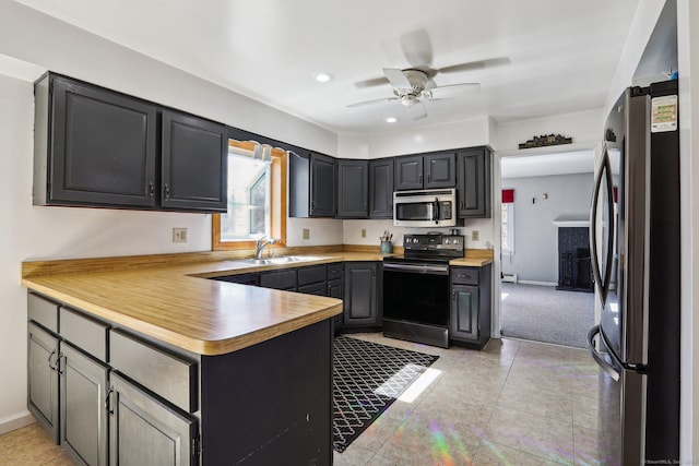 kitchen with a ceiling fan, a peninsula, a sink, light countertops, and appliances with stainless steel finishes