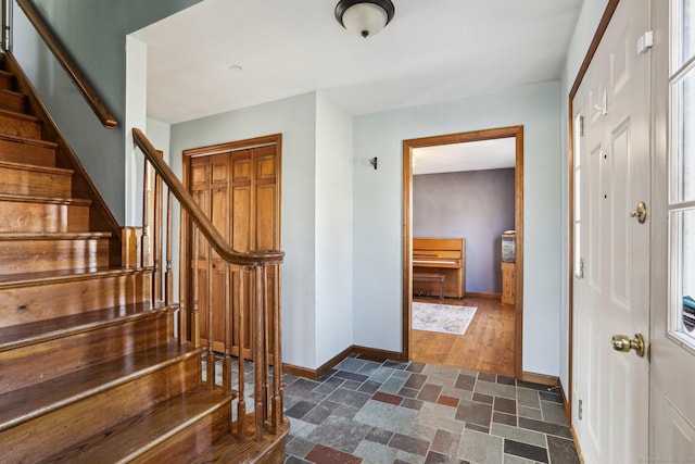 foyer entrance with stairs, stone finish floor, and baseboards