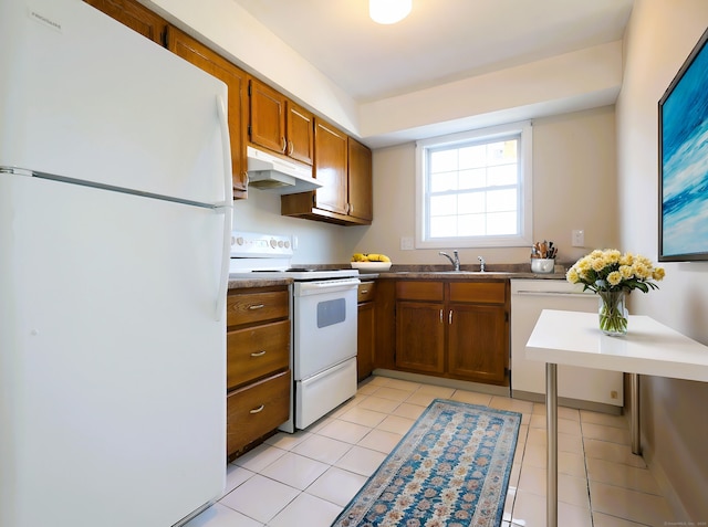 kitchen with under cabinet range hood, light tile patterned floors, brown cabinetry, white appliances, and a sink