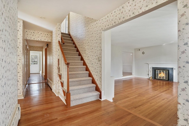 staircase with a baseboard radiator, a baseboard heating unit, wood finished floors, and wallpapered walls