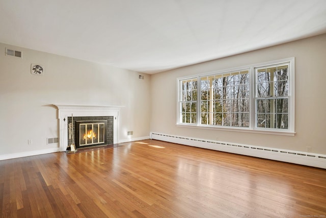 unfurnished living room featuring baseboard heating, a fireplace with flush hearth, visible vents, and wood finished floors