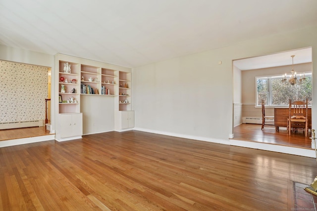 unfurnished living room with a notable chandelier, baseboard heating, and wood finished floors