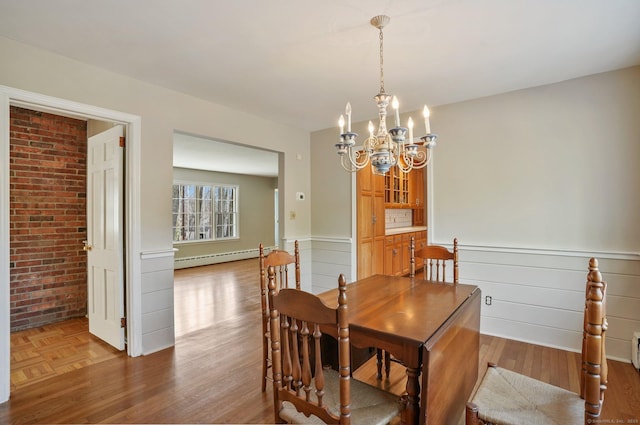 dining space featuring brick wall, parquet flooring, wainscoting, an inviting chandelier, and a baseboard radiator