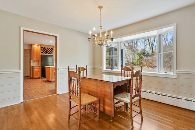 dining space featuring wainscoting, a chandelier, light wood-style flooring, and a baseboard radiator