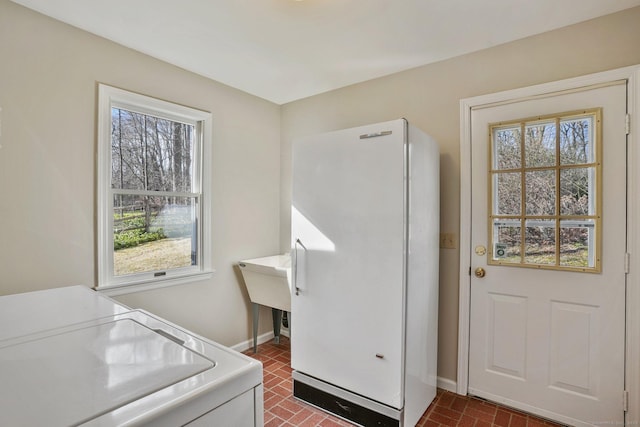 laundry room featuring laundry area, plenty of natural light, separate washer and dryer, and brick floor