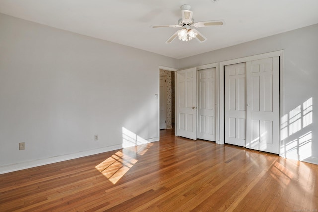 unfurnished bedroom with baseboards, multiple closets, wood finished floors, and a ceiling fan