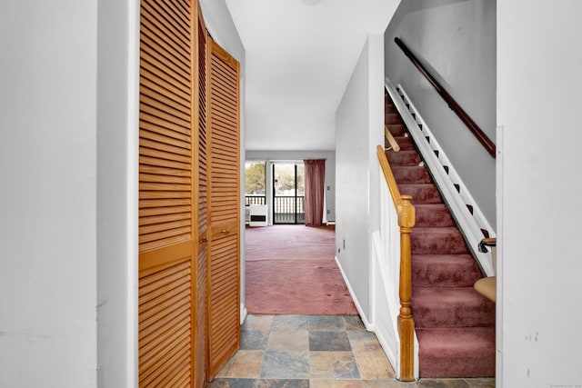 hallway featuring stairway, stone finish floor, baseboards, and carpet