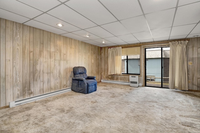 unfurnished room featuring a drop ceiling, baseboard heating, wooden walls, and carpet