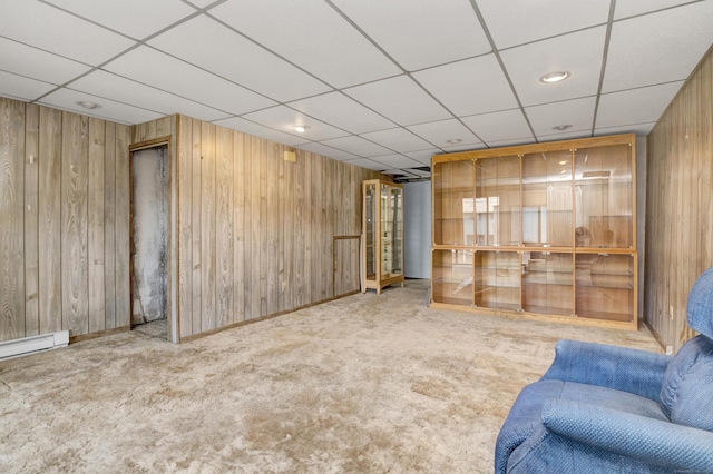 unfurnished living room with wooden walls, a baseboard heating unit, a paneled ceiling, and carpet floors