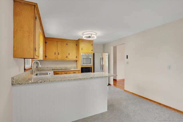 kitchen featuring a sink, light colored carpet, stainless steel appliances, baseboards, and a peninsula