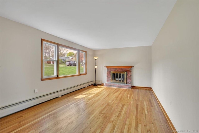 unfurnished living room with baseboard heating, baseboards, hardwood / wood-style floors, and a brick fireplace