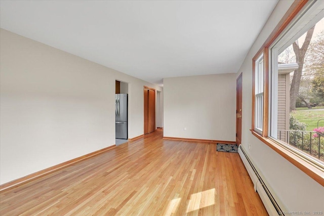 empty room with baseboards, baseboard heating, and light wood-type flooring