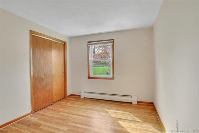 unfurnished bedroom with light wood-style floors, a closet, a baseboard heating unit, and baseboards
