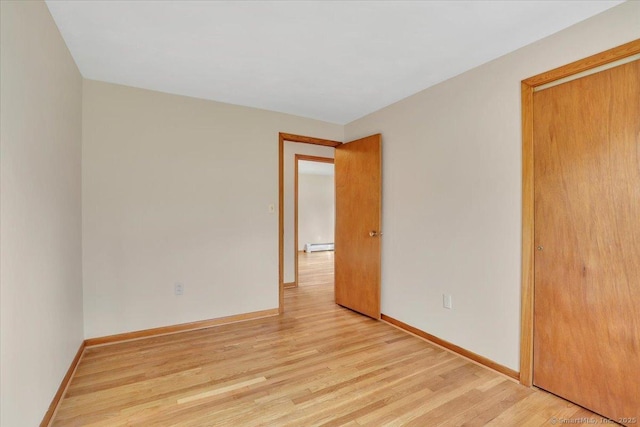 unfurnished bedroom with a closet, a baseboard radiator, light wood-style flooring, and baseboards