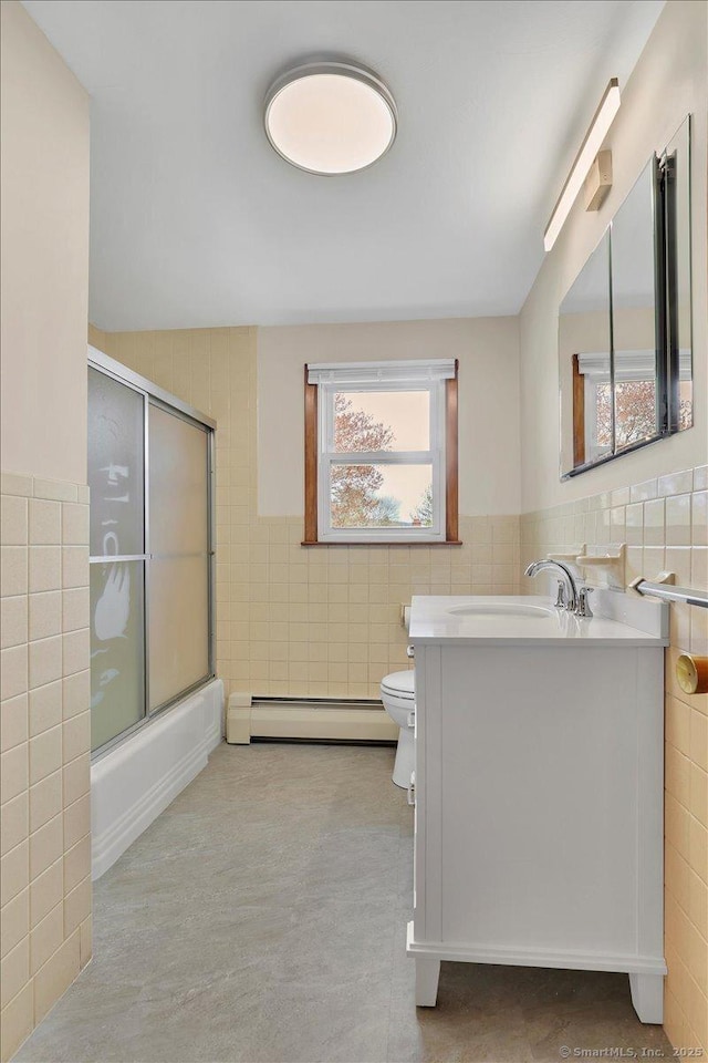 bathroom with a baseboard radiator, tile walls, shower / bath combination with glass door, toilet, and vanity