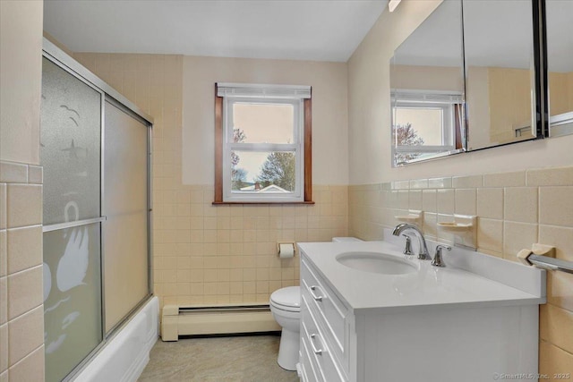 bathroom featuring tile walls, vanity, toilet, combined bath / shower with glass door, and baseboard heating