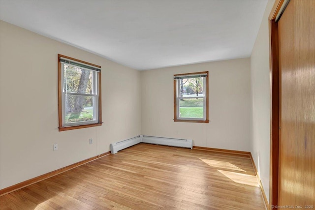 spare room featuring light wood finished floors, baseboard heating, and baseboards