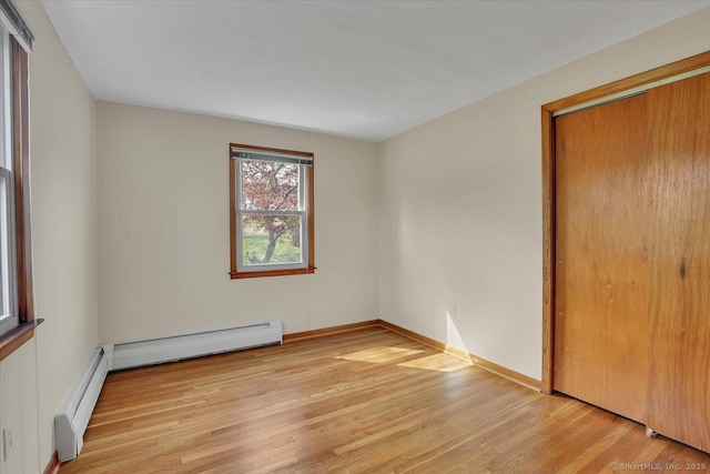 unfurnished bedroom featuring baseboards, a baseboard heating unit, a closet, and light wood-style flooring