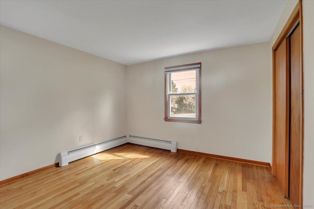 unfurnished bedroom featuring a baseboard radiator, a closet, light wood-style flooring, and baseboards