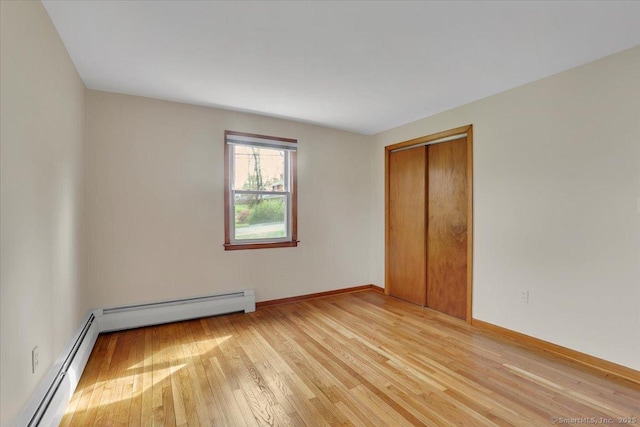 unfurnished bedroom with baseboards, light wood-style flooring, baseboard heating, and a closet