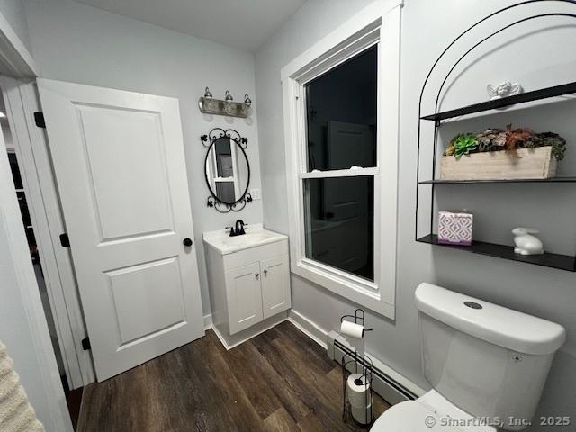 half bath featuring vanity, wood finished floors, baseboards, a baseboard radiator, and toilet