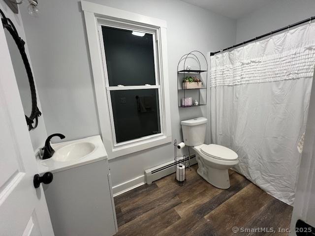 bathroom featuring a baseboard heating unit, toilet, a shower with curtain, wood finished floors, and vanity