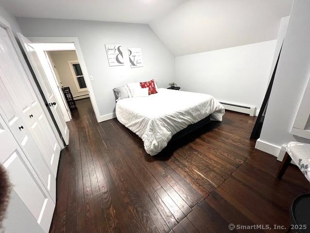 bedroom featuring a baseboard heating unit, lofted ceiling, baseboards, and dark wood-style floors