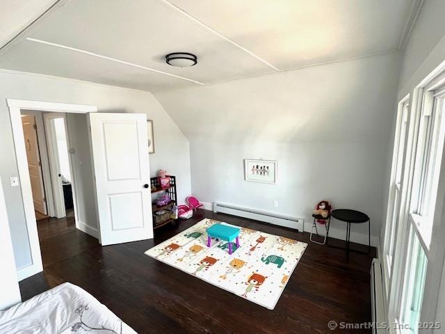 recreation room featuring dark wood finished floors, a baseboard heating unit, baseboards, and vaulted ceiling