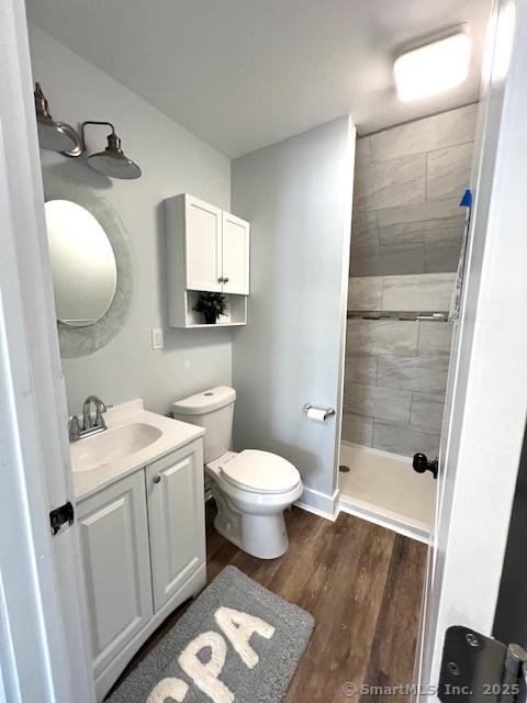 bathroom with vanity, toilet, wood finished floors, and tiled shower