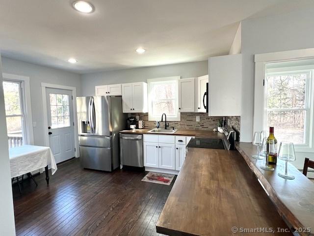 kitchen with decorative backsplash, dark wood-style floors, white cabinets, stainless steel appliances, and a sink