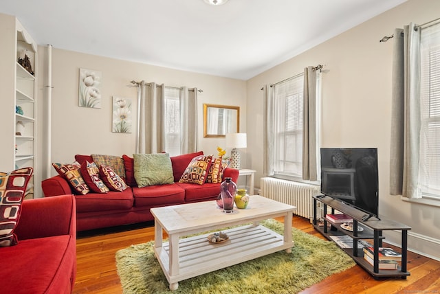 living area with a wealth of natural light, baseboards, wood finished floors, and radiator heating unit