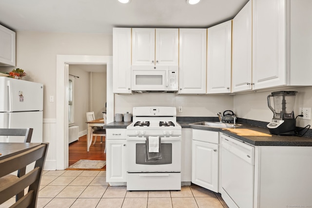 kitchen with a sink, dark countertops, white cabinetry, white appliances, and light tile patterned floors