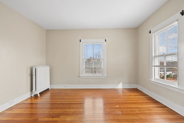 empty room featuring a wealth of natural light, wood finished floors, and radiator heating unit