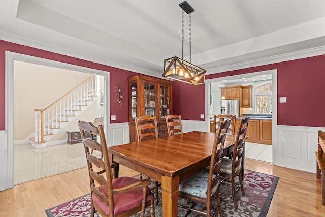 dining room with a wainscoted wall, stairs, light wood-style floors, and ornamental molding