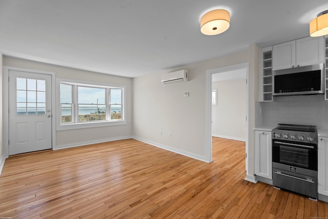 kitchen with a wall unit AC, light countertops, light wood-style floors, appliances with stainless steel finishes, and backsplash