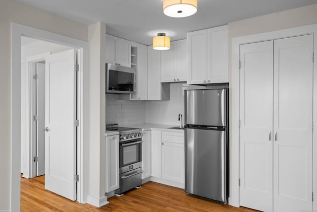 kitchen with white cabinetry, stainless steel appliances, light wood-type flooring, and light countertops