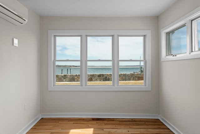 unfurnished room with a wall mounted air conditioner, baseboards, a water view, and light wood-style flooring