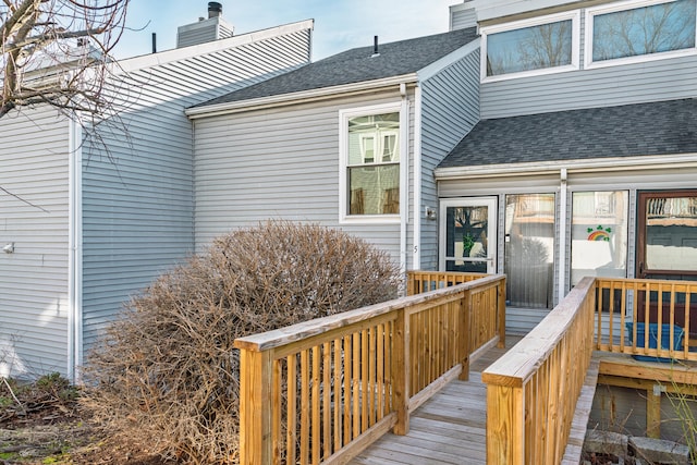 property entrance with a wooden deck, roof with shingles, and a chimney